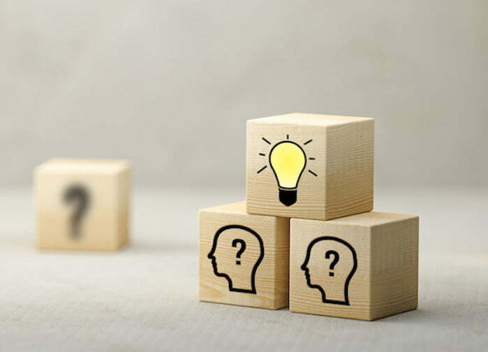 Wooden blocks with a glowing light bulb on top, symbolizing creativity, and two people engaged in thoughtful discussion, representing brainstorming for innovative advertising ideas.