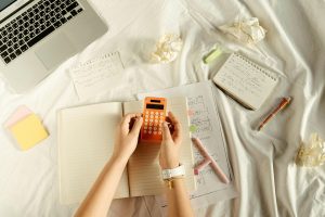 Image shows someone using a calculator that is above some pieces of paper and a notebook